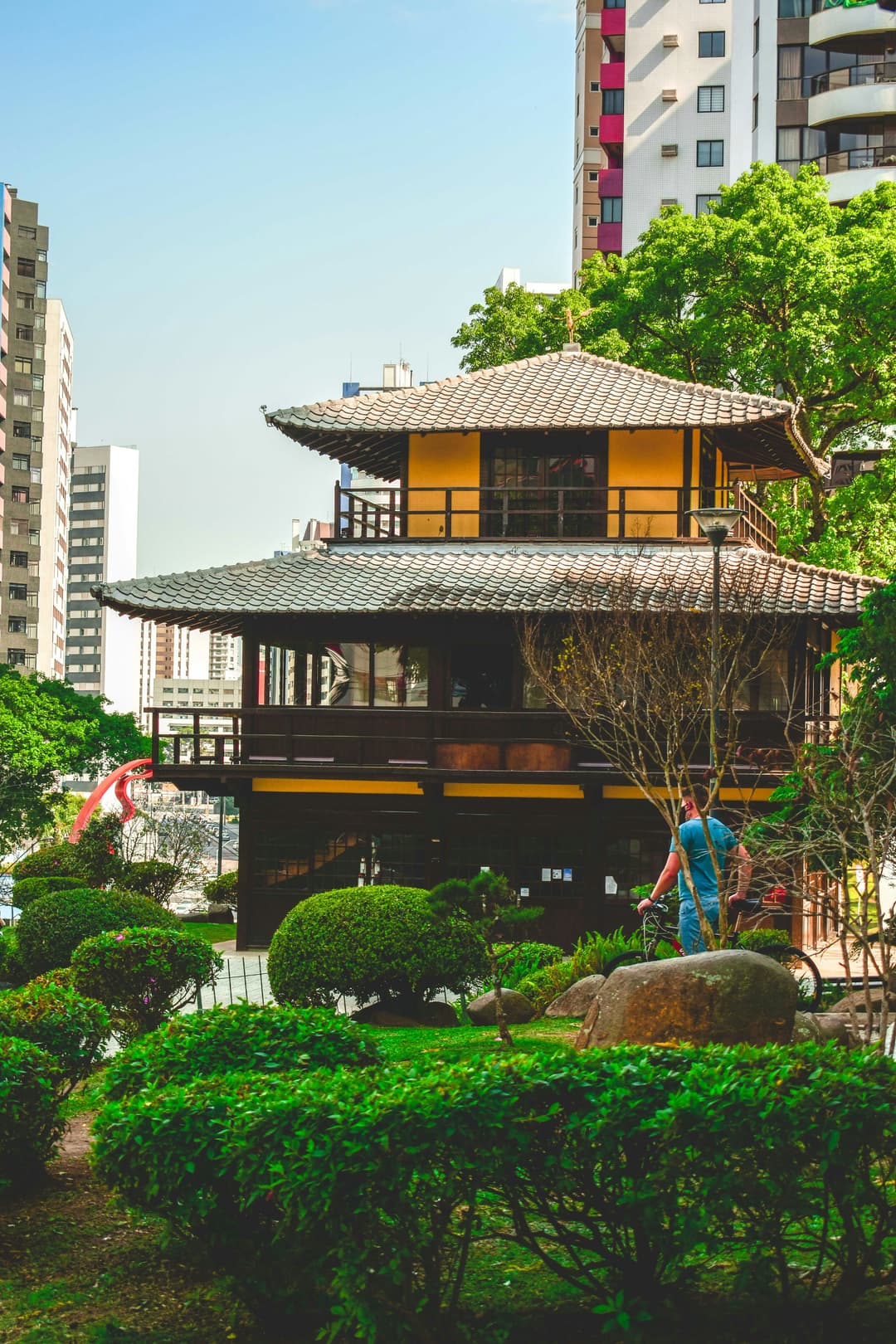 Monumento tradicional japonês na Praça do Japão, localizado no bairro Batel em Curitiba, cercado por vegetação e com edifícios modernos ao fundo, representando a harmonia entre cultura e urbanização.